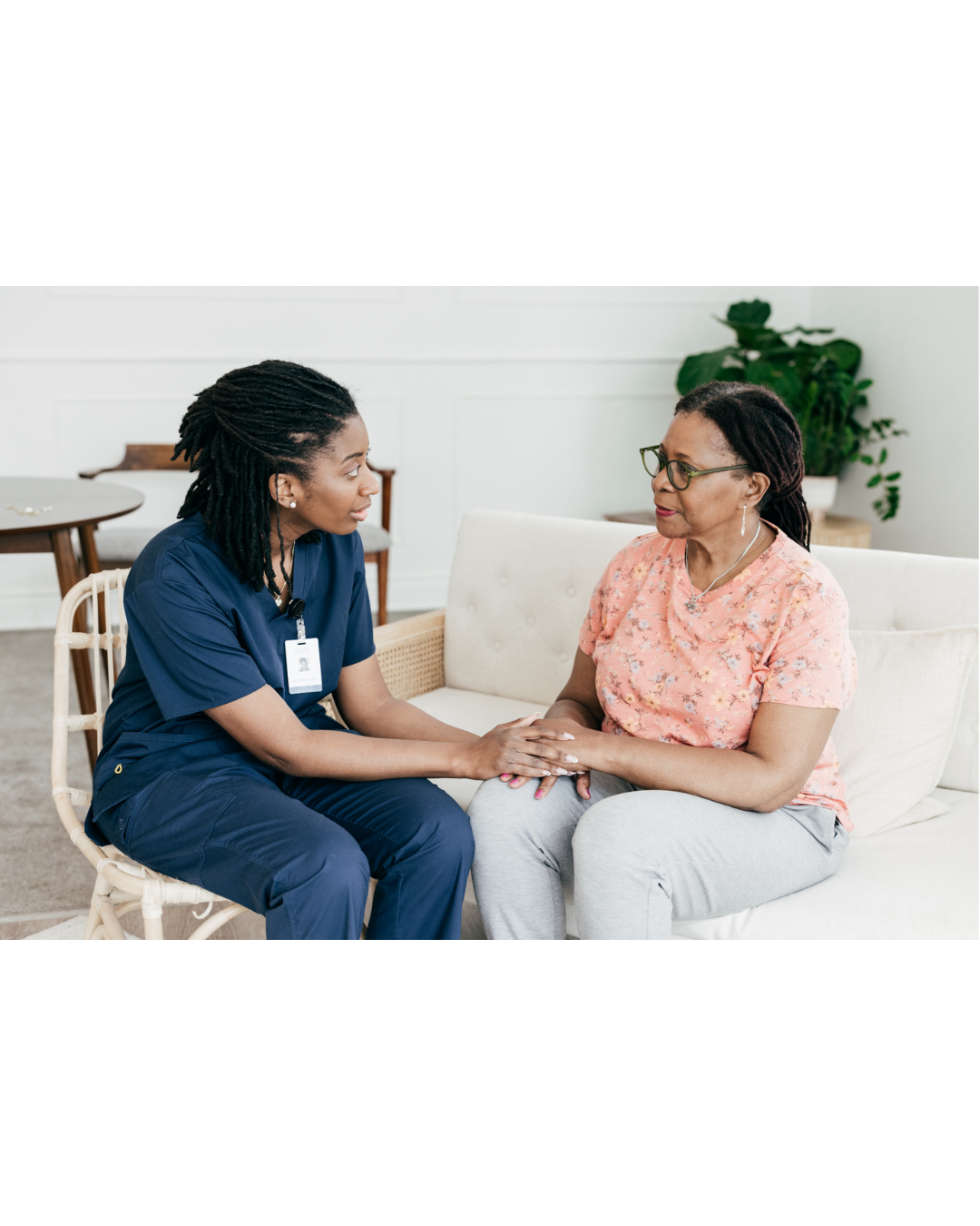 A health care professional and a patient holding hands while sitting together.